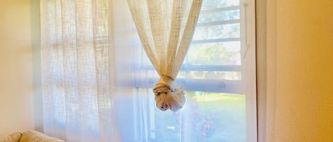 Un dormitorio con cama, ventana con cortinas traslúcidas y vistas al exterior.
