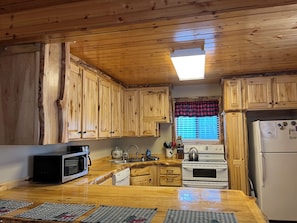 A kitchen with wooden cabinets, a microwave, a stove, and a refrigerator. - Centennial Chalet , Tranquil cabin 20 min from Yellowstone (Island Park)