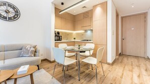 A modern living room with a sofa, dining table, and chairs, a kitchen in the background, and a clock on the wall. - Modern Studio in Oakley Square JVC with Pool, Gym & Cinema (Dubai)