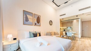A modern hotel room with a large bed, a desk, and a kitchenette. - Modern Studio in Oakley Square JVC with Pool, Gym & Cinema (Dubai)