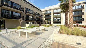 A modern building with multiple balconies, outdoor seating areas, and a palm tree. - Modern Studio in Oakley Square JVC with Pool, Gym & Cinema (Dubai)