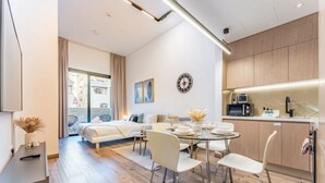 A modern hotel room with a dining area, a kitchen, and a large window with a view of the city. - Modern Studio in Oakley Square JVC with Pool, Gym & Cinema (Dubai)