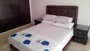 A bedroom with a bed, a nightstand, a dark wooden wardrobe, and a white wall. - Apartment Gueliz - Near ONCF station - Marrakech (Marrakech)