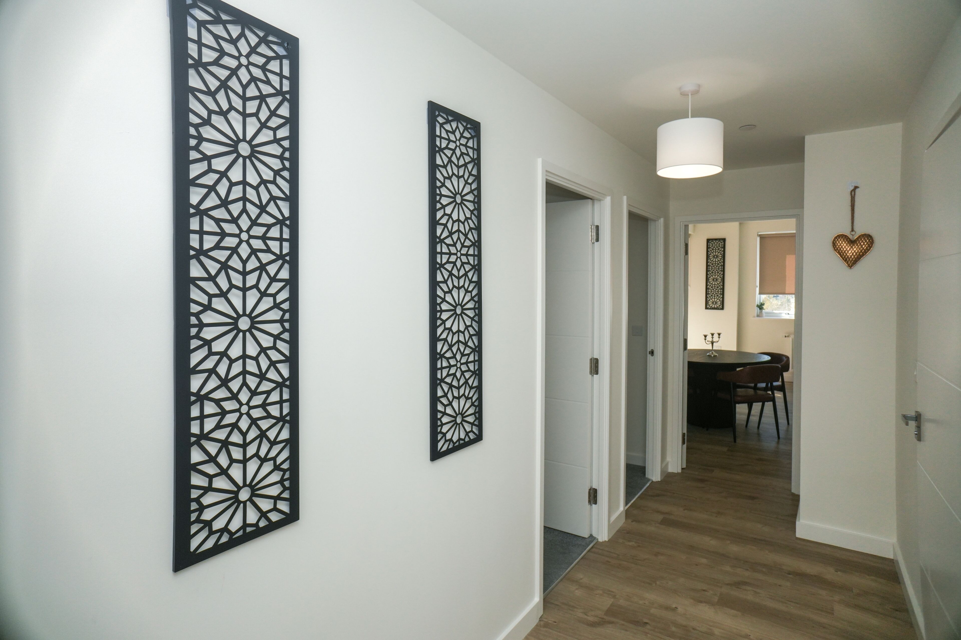 Een gang met twee zwarte decoratieve panelen, een witte plafondlamp en een eethoek op de achtergrond.