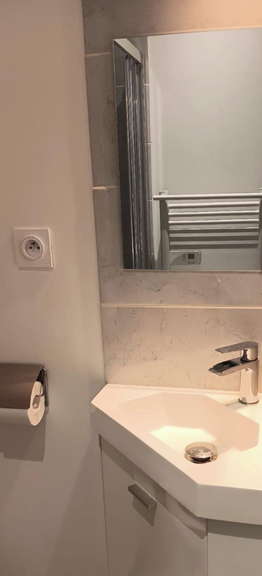 Un baño con lavamanos blanco, espejo y dispensador de papel higiénico.