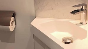 Un baño con lavamanos blanco, espejo y dispensador de papel higiénico.