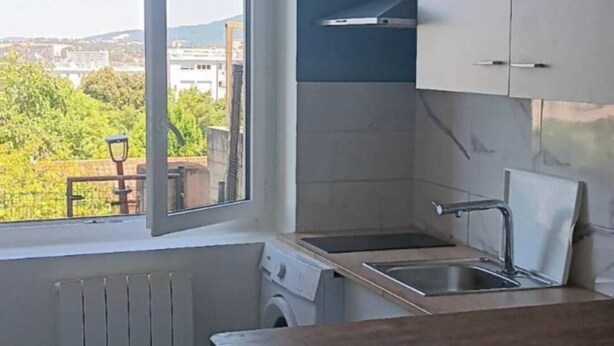 Una cocina con ventana, armarios blancos, un lavamanos y una lavadora.