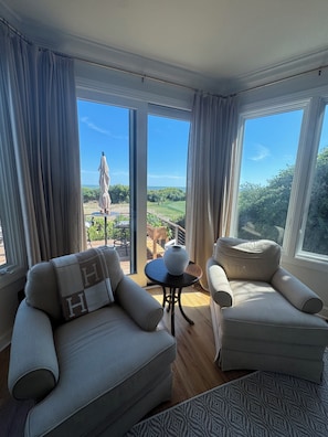 Une pièce avec deux canapés, une petite table et une vue sur un jardin et le ciel, grâce à de grandes fenêtres.