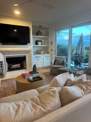 A living room with a fireplace, a flat-screen TV, a sofa, and a view of the outdoors.
