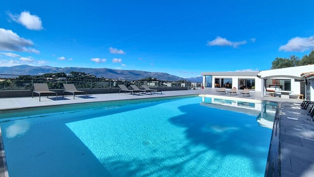 Une piscine sur le toit, avec une eau d’un bleu limpide, entourée de chaises longues et bordée d’un bâtiment moderne aux grandes fenêtres.