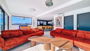 Un salon moderne avec des canapés rouges, une table basse en bois et une vue sur les montagnes grâce à de grandes fenêtres.