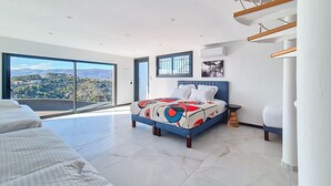 Une chambre avec un grand lit, une vue sur le paysage urbain et un escalier moderne.