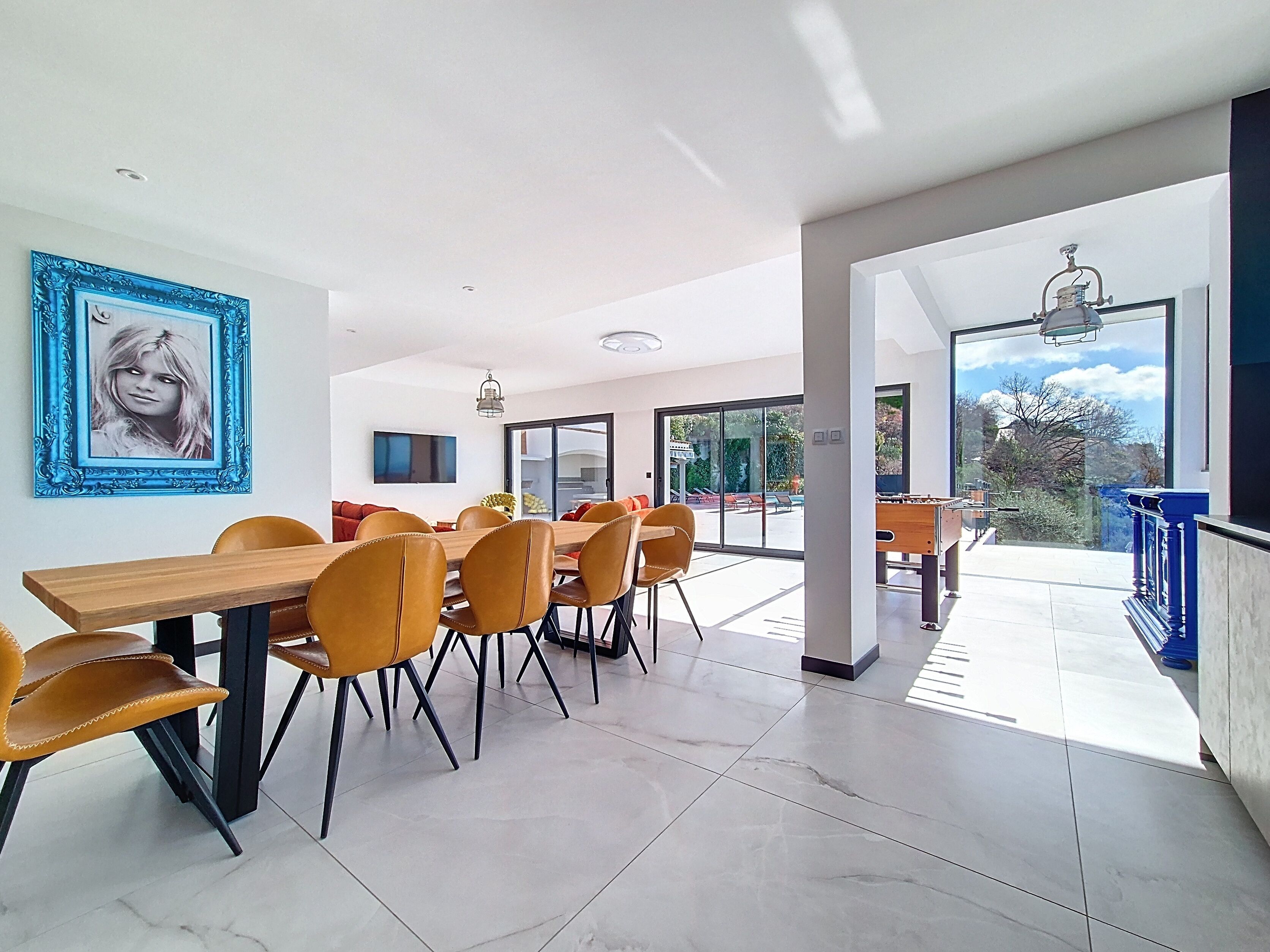 A modern dining area with a long table and chairs, a large window, and a view of the outdoors.