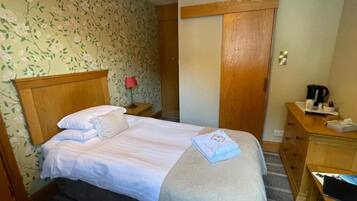 A hotel room with a bed, a desk, a chair, a nightstand, a red lamp, and a wooden wardrobe.