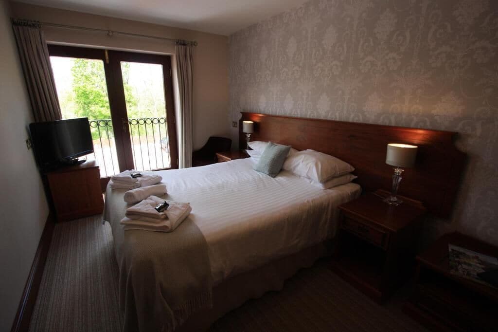 Habitación de hotel con cama, televisión, mesita de noche, lámpara y vistas al exterior.