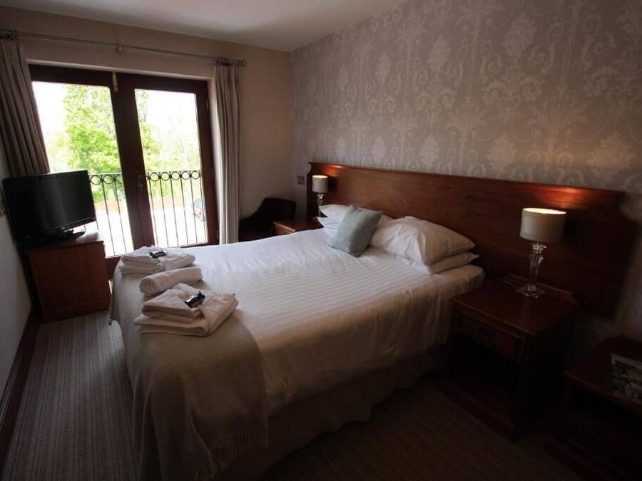A hotel room with a bed, a TV, a nightstand, a lamp, and a view through the window.
