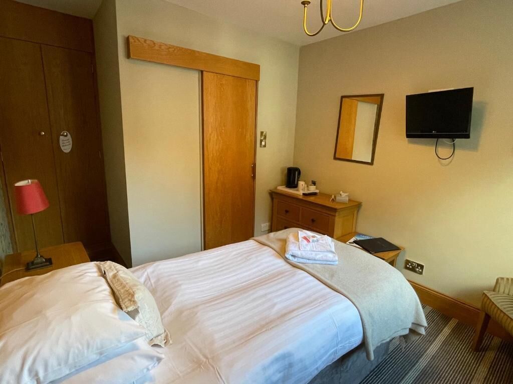Une chambre d’hôtel avec un lit, une armoire en bois, un téléviseur fixé au mur et une petite table avec une lampe.