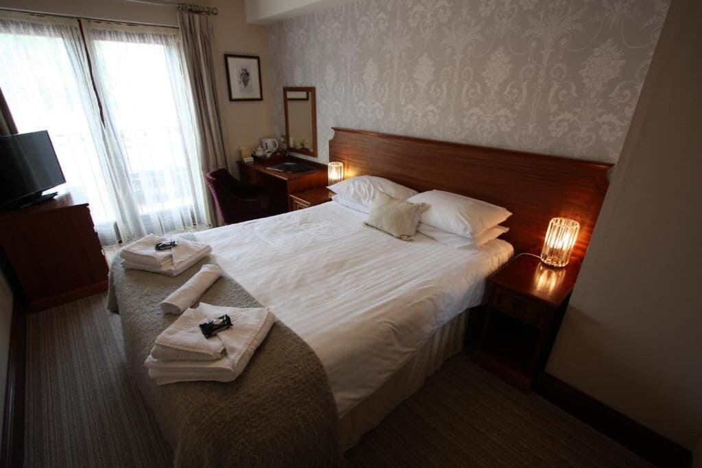 Habitación de hotel con cama bien hecha, un escritorio con lámpara, televisión y ventana con cortinas.
