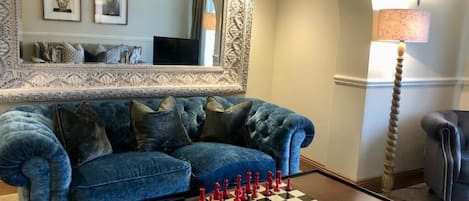 Una sala de estar con un sofá azul, un tablero de ajedrez, un espejo y una lámpara.