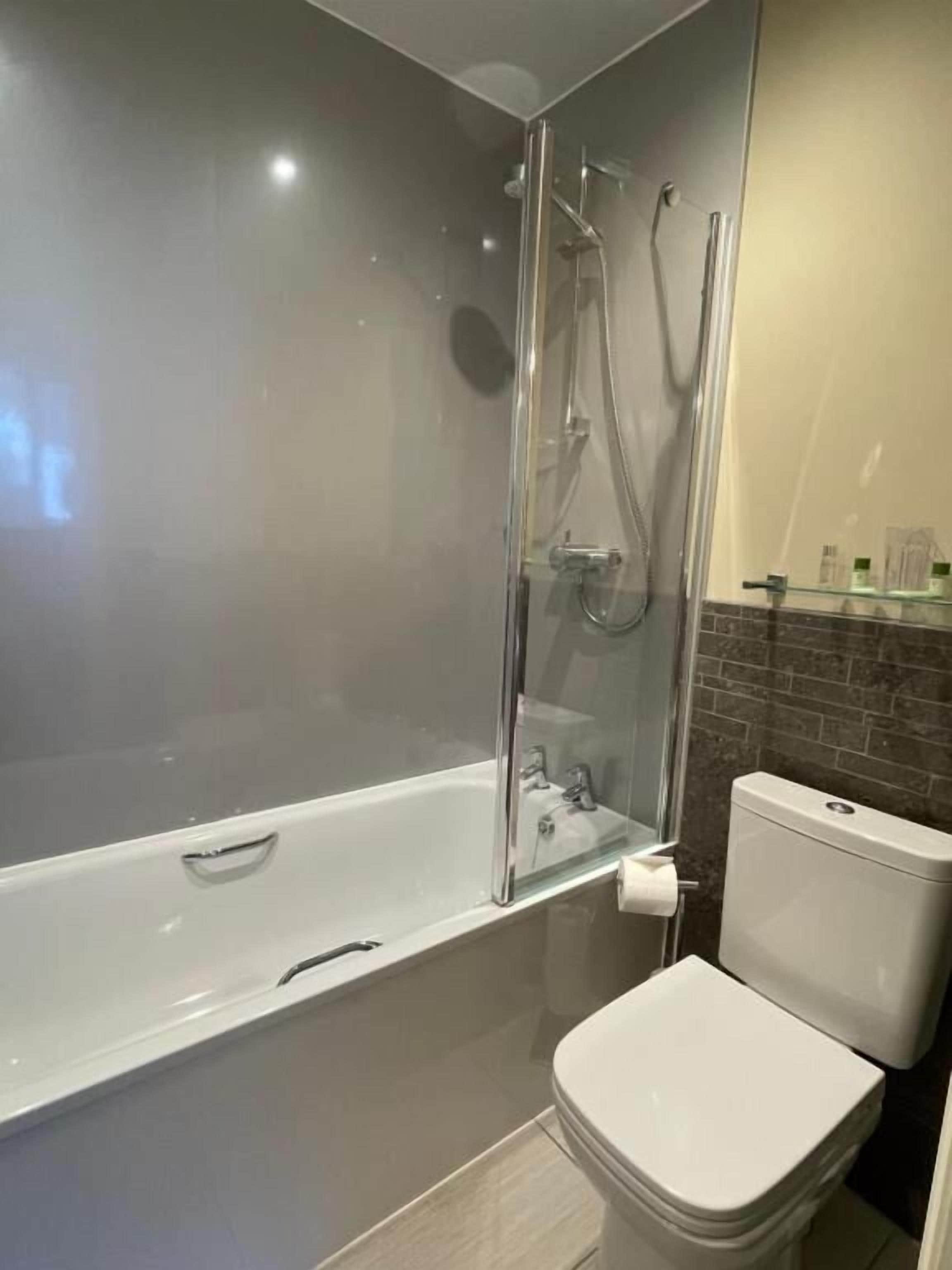 A modern bathroom with a glass-enclosed shower, a white bathtub, and a toilet.