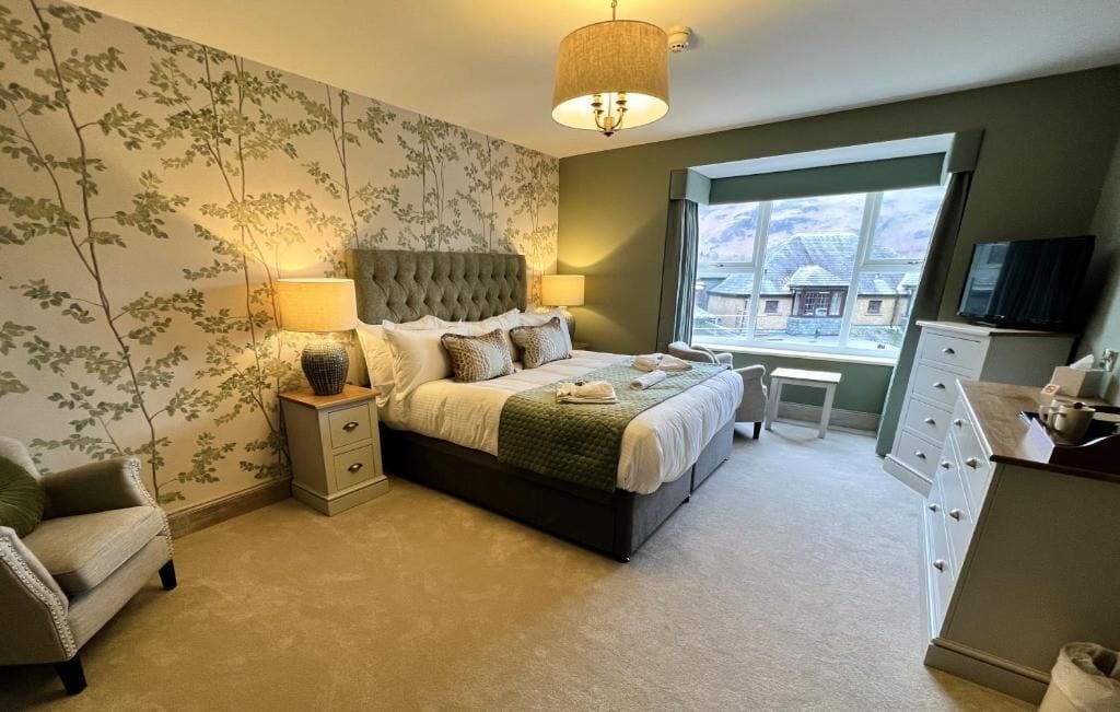 A bedroom with a large bed, bedside tables, a chair, a dresser, and a window with a view.