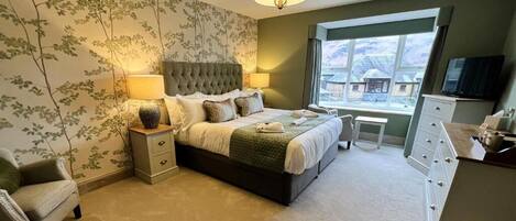 A bedroom with a large bed, bedside tables, a chair, a dresser, and a window with a view.