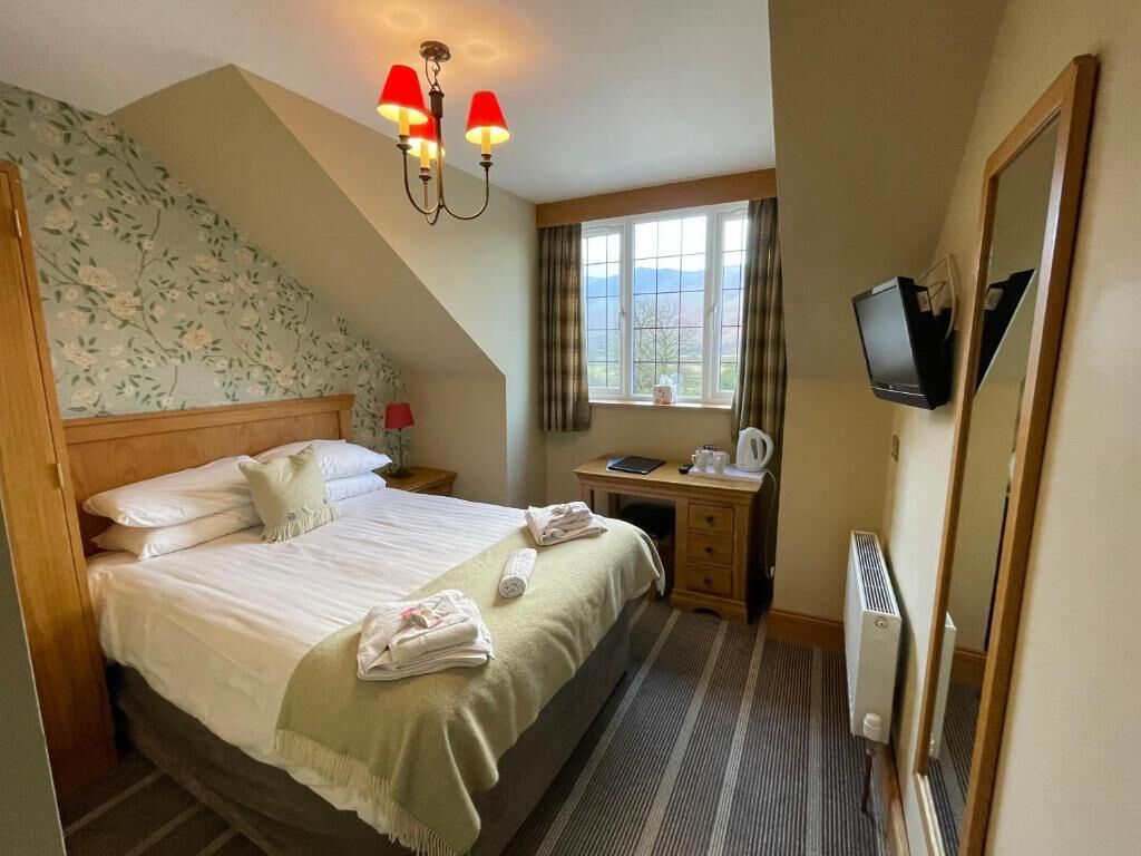A hotel room with a bed, a desk with a computer, a television, and a window with curtains.