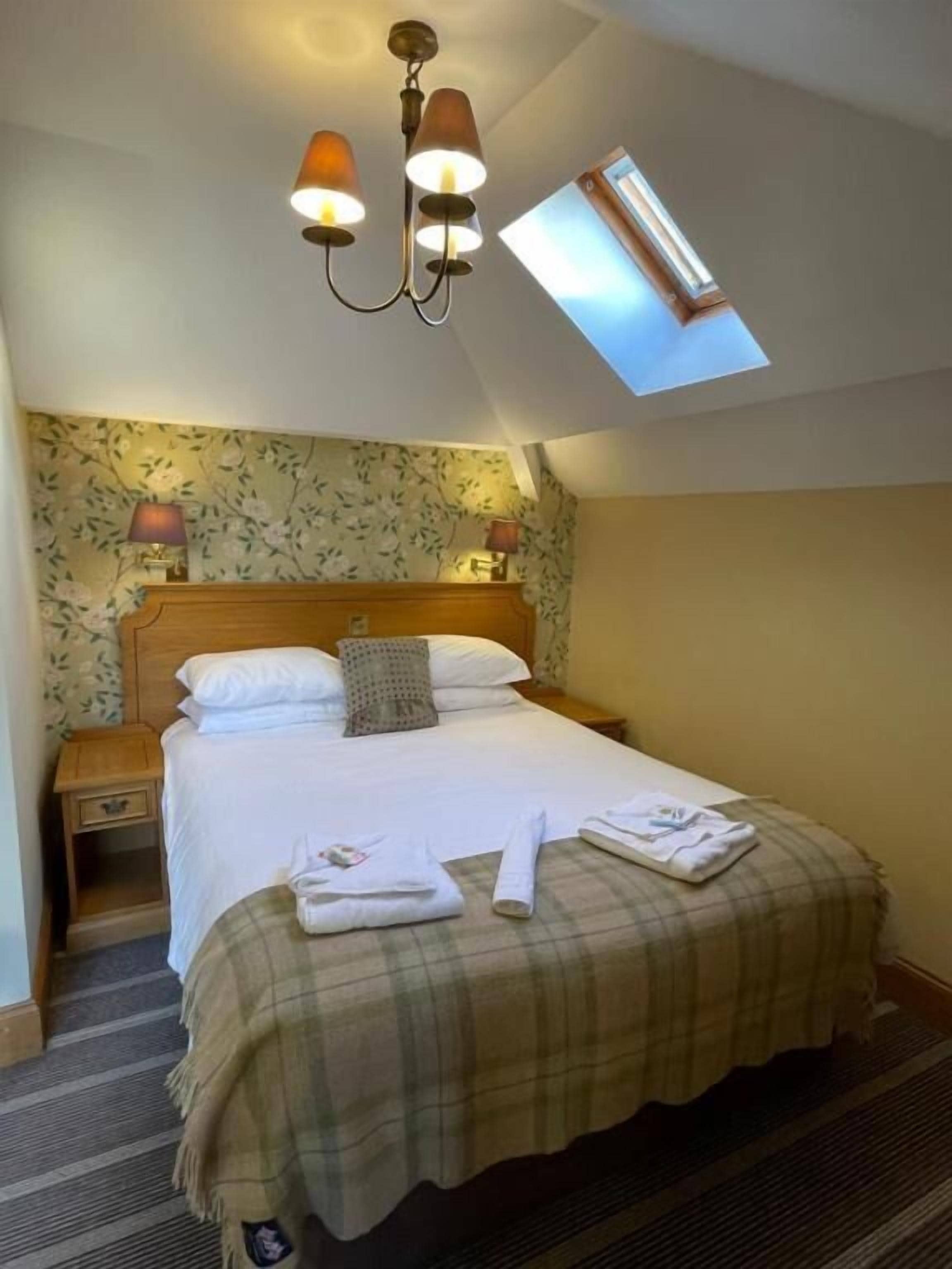 A hotel room with a bed, a nightstand, a lamp, a window, and a ceiling light fixture.