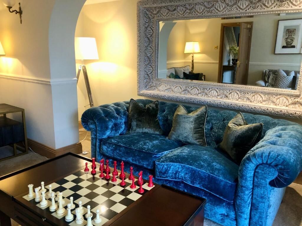 A living room with a checkered chessboard, a blue velvet sofa, and a large ornate mirror.