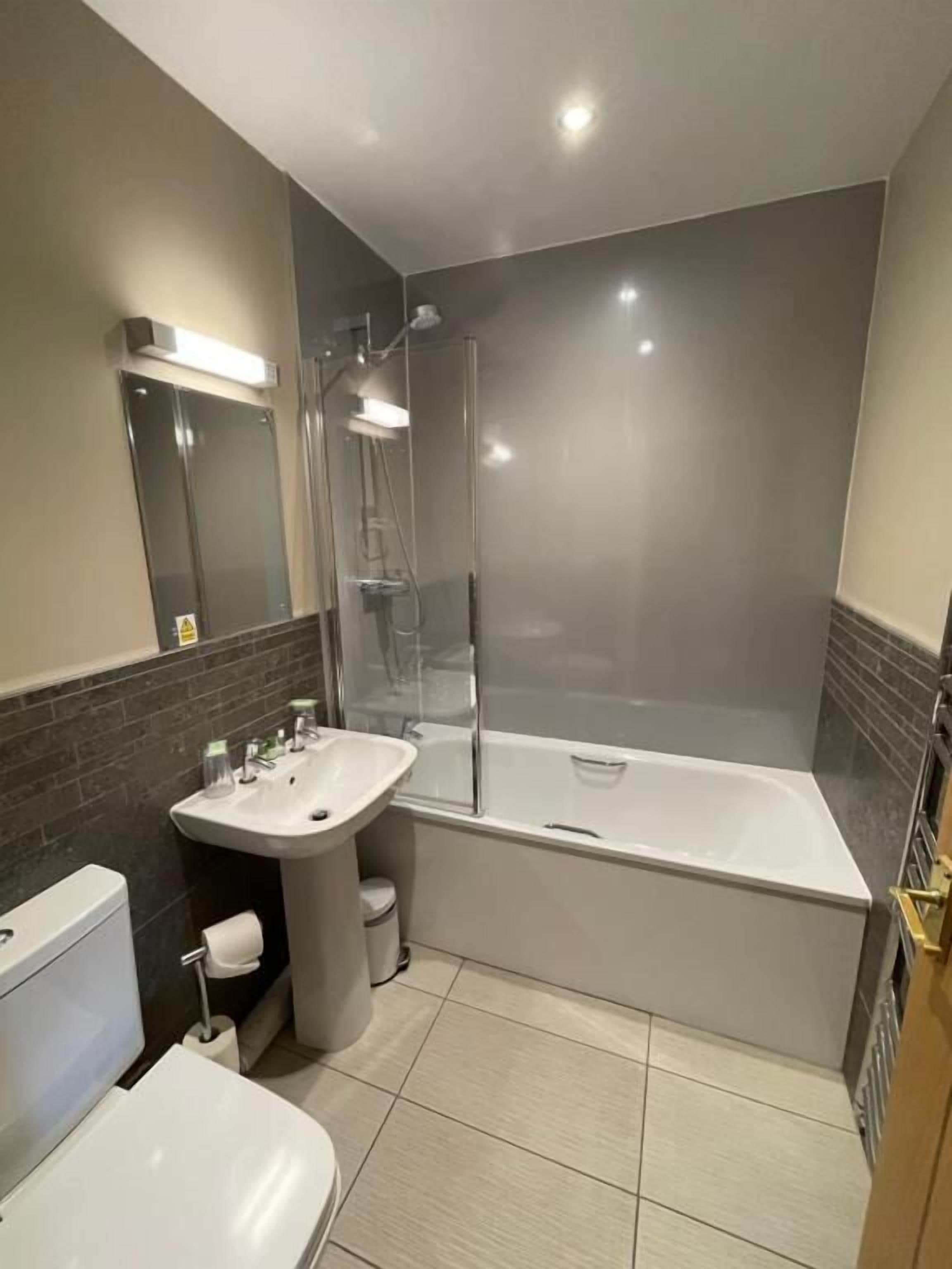A modern bathroom with a glass-enclosed shower, a white bathtub, a sink with a mirror, and a toilet.