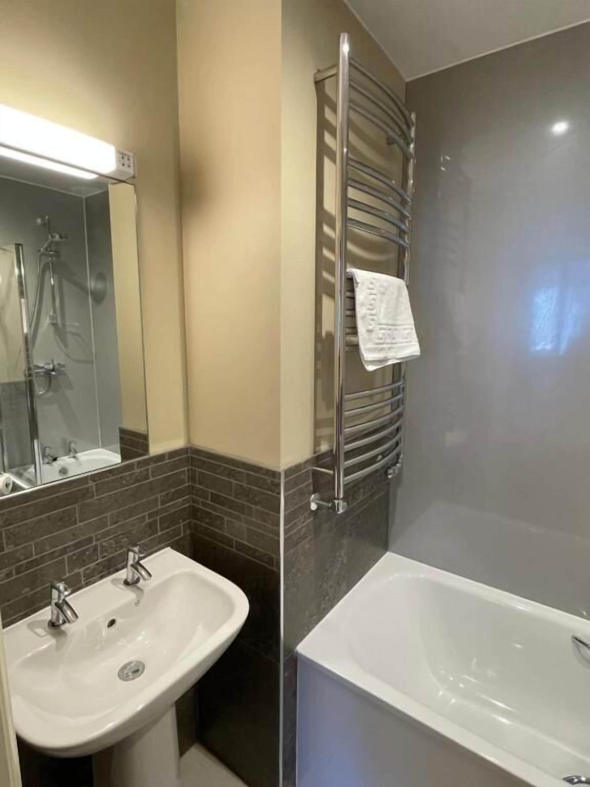 Un baño con dos lavamanos, una bañera, un perchero y una ducha.
