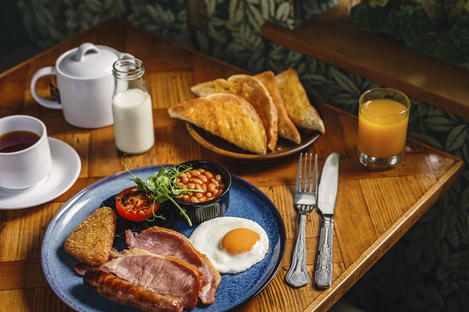 A breakfast tray with toast, eggs, beans, ham, and a glass of orange juice.