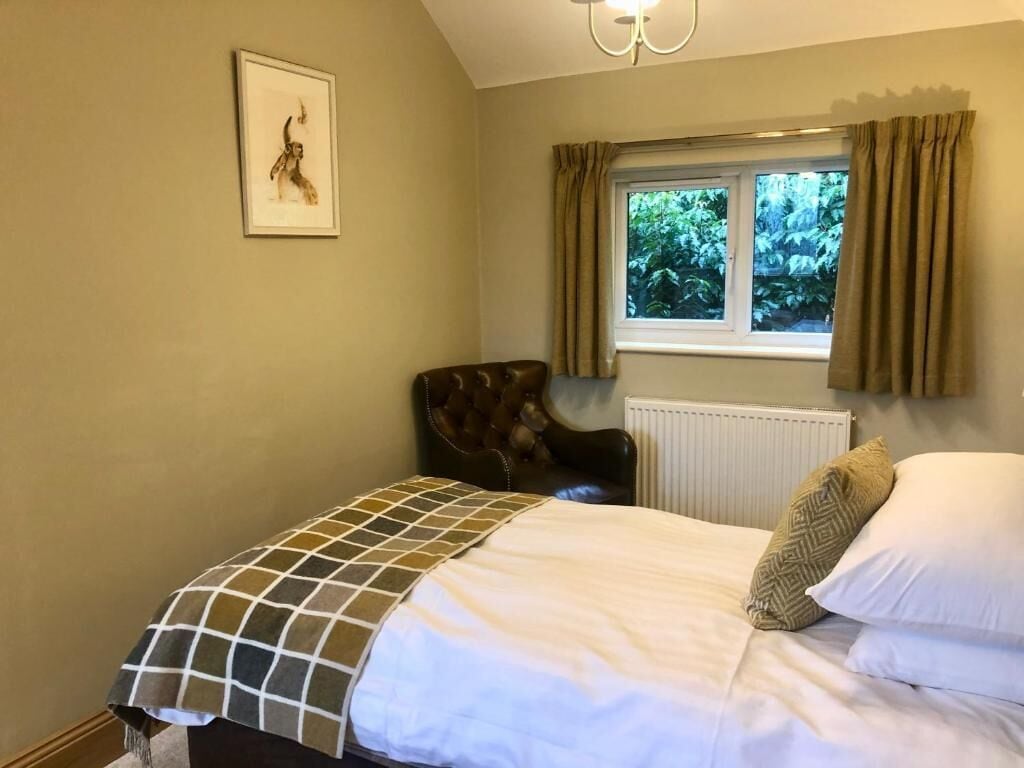 Une chambre à coucher avec un lit, une chaise, une fenêtre avec des rideaux et un radiateur.
