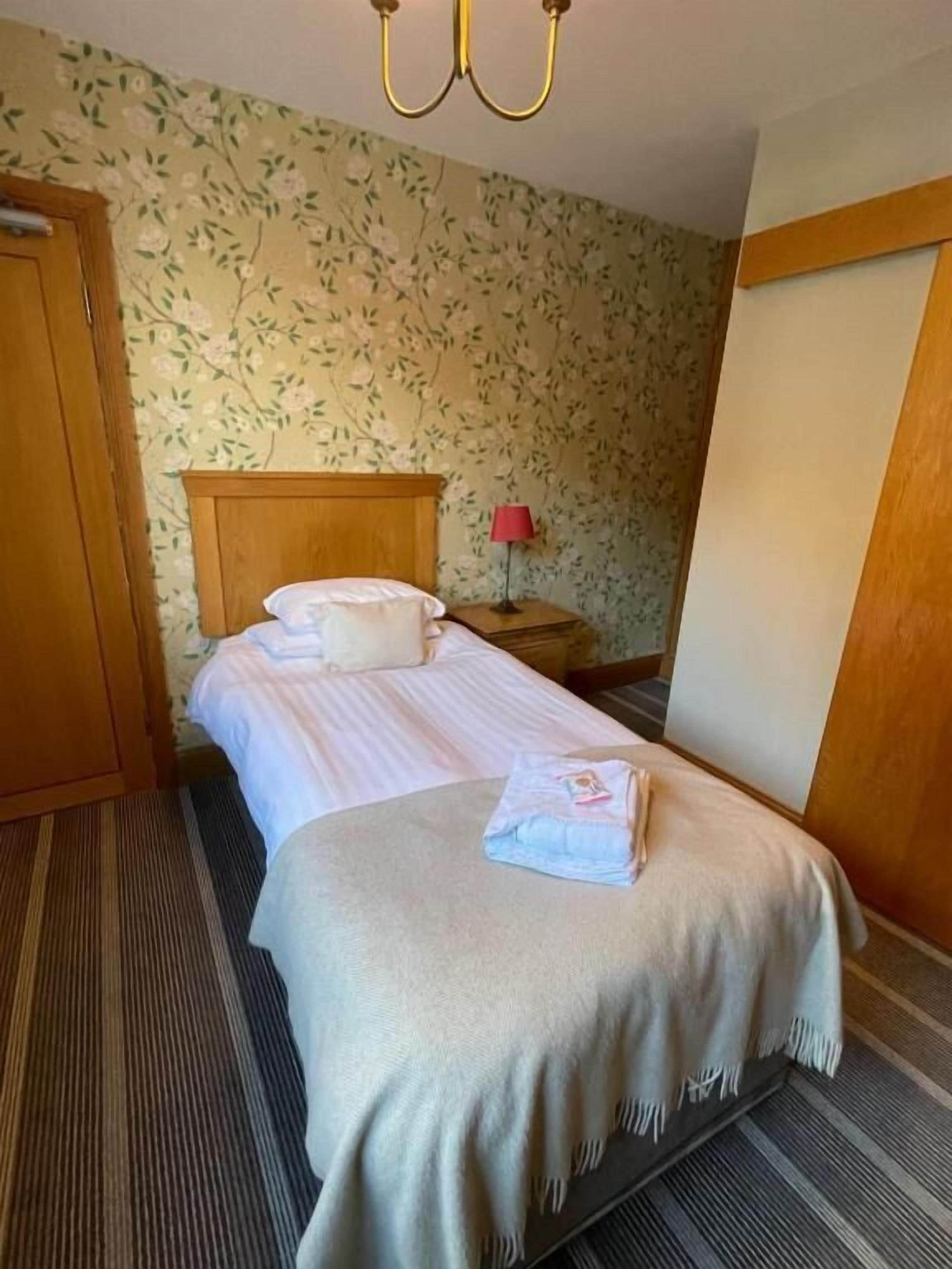 Uma cama bem arrumada com cabeceira, abajur e toalha dobrada sobre a cama.