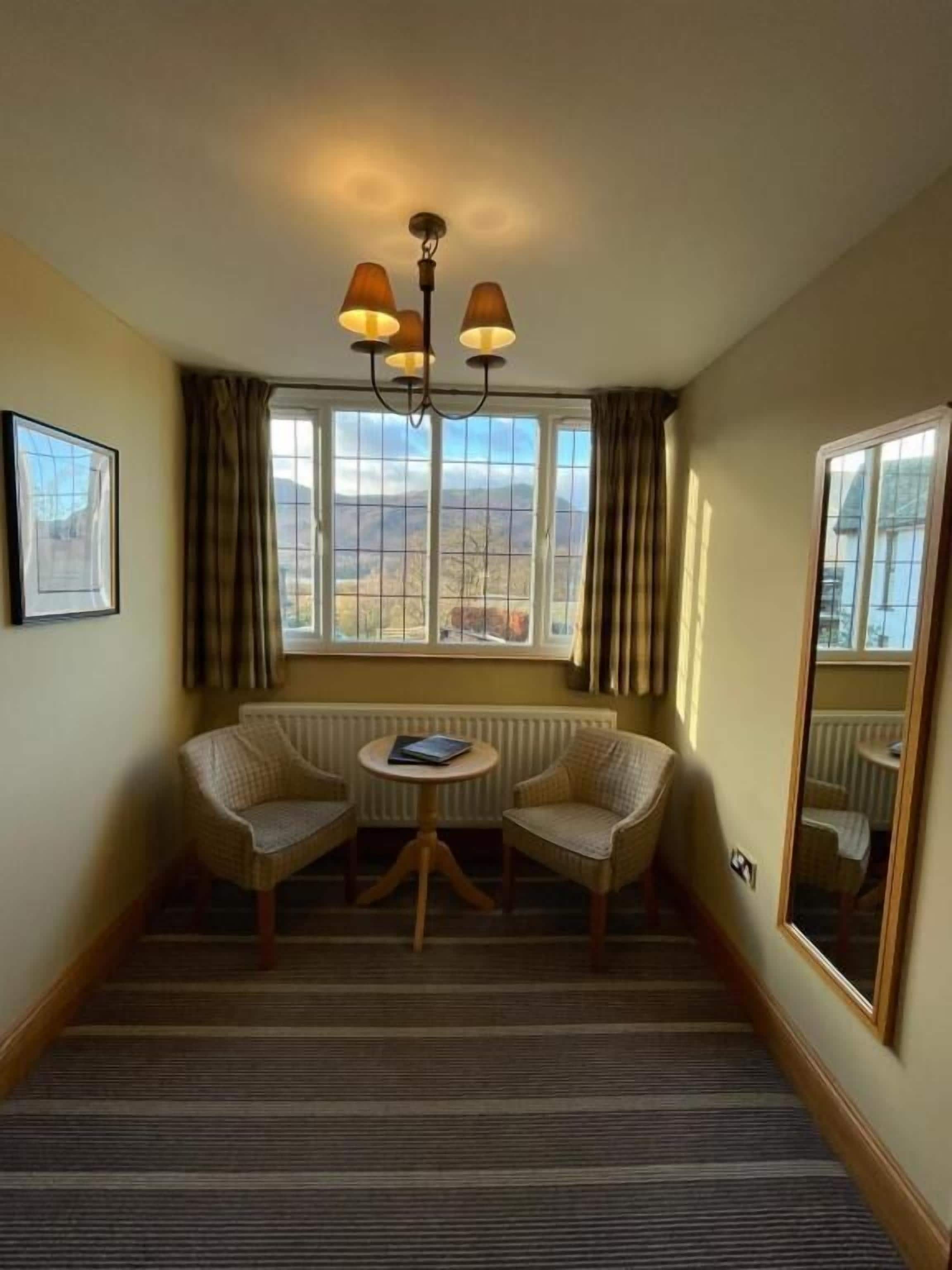 Une chambre d’hôtel avec vue sur les montagnes, un lustre, deux fauteuils, une petite table et un radiateur.