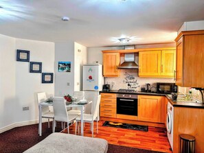A compact kitchen with wooden cabinets, a built-in oven, and a dining area with a table and chairs. - Contractor-friendly 2BR Gem Wi-fi & Free Parking (Warrington)