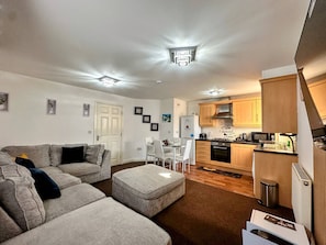 A compact living space with a grey sofa, a dining table with chairs, a kitchenette with wooden cabinets, and a white door. - Contractor-friendly 2BR Gem Wi-fi & Free Parking (Warrington)