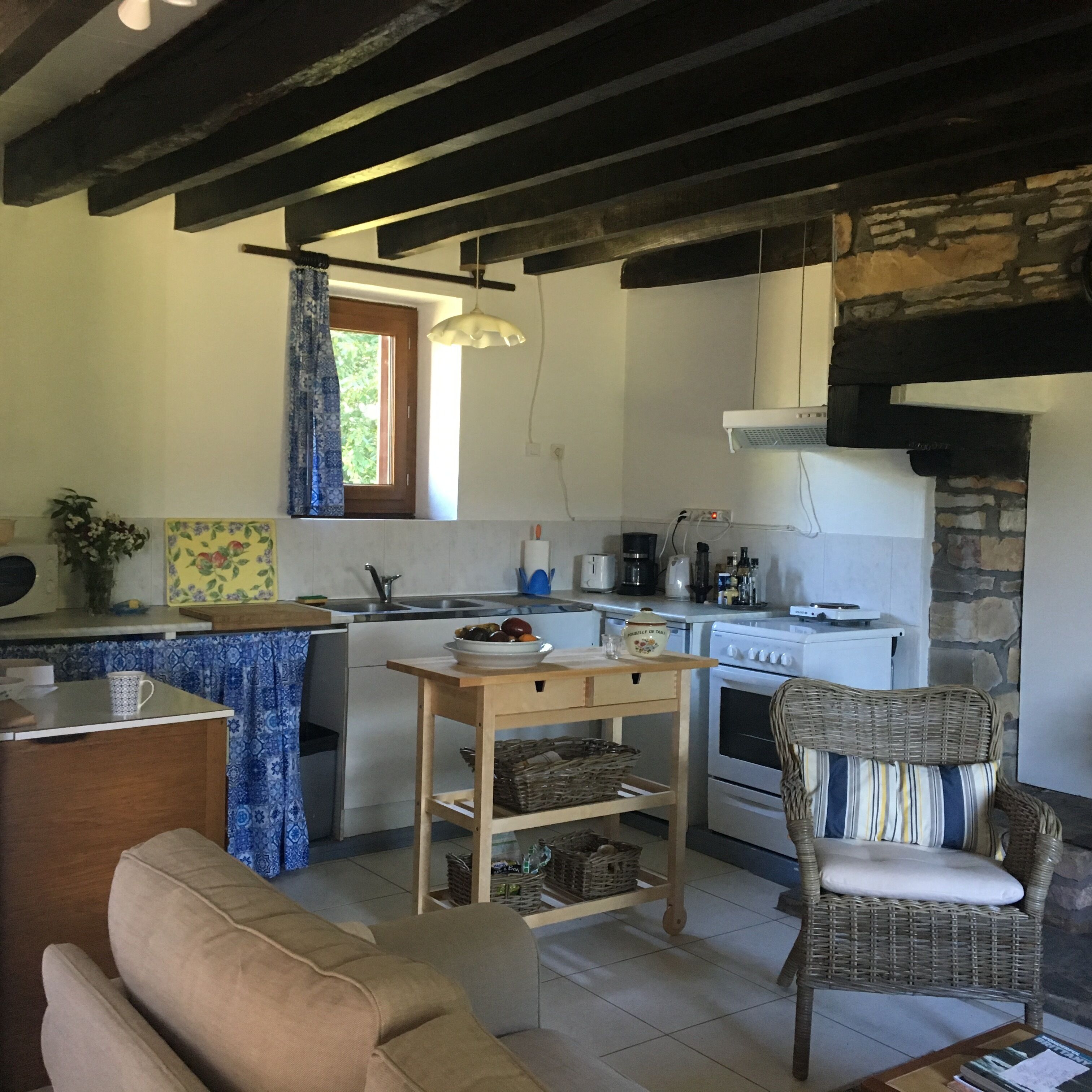 Una cocina con una isla central, estufa y comedor con una silla de mimbre.
