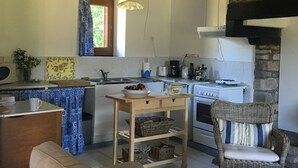 A kitchen with a central island, a stove, and a dining area with a wicker chair. - Delightful 2-bedroom cottage perfect for a revitalizing retreat in Brittany (Ruffiac)