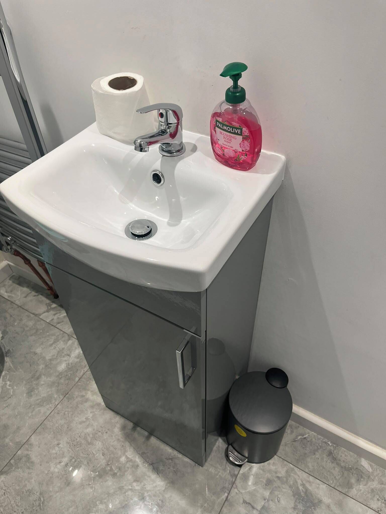 Ein Badezimmerwaschbecken mit einer Toilettenpapierrolle, einem Seifenspender und einem Mülleimer.