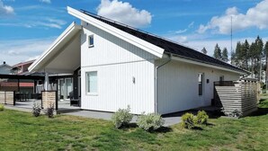 Un edificio moderno de color blanco con techo inclinado, un área de estar al aire libre cubierta y un pequeño jardín.