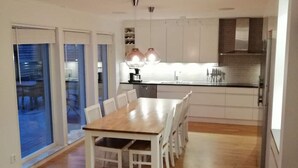 Una cocina moderna con armarios blancos, una mesa de comedor de madera y un amplio ventanal con vistas a un balcón.