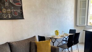 Ein modernes Wohnzimmer mit einem grauen Sofa, einem runden Metall-Couchtisch und einem Essbereich mit weißem Tisch und schwarzen Stühlen.