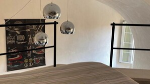 Ein Schlafzimmer mit gewölbter Decke, einem Bett mit gestreifter Bettdecke, einer Wandillustration mit einem Fisch und drei hängenden Kugelspeigeln.