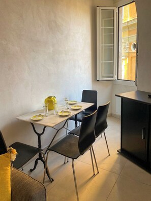 A dining area with a table set for four, chairs, a cabinet, and a window with a view of the outside. - Chic Ferrié Riviera apartment (Menton)