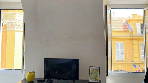 Ein Zimmer mit einem modernen Kronleuchter, einem Flachbildfernseher und einem Fenster mit Blick auf gelbe Gebäude.