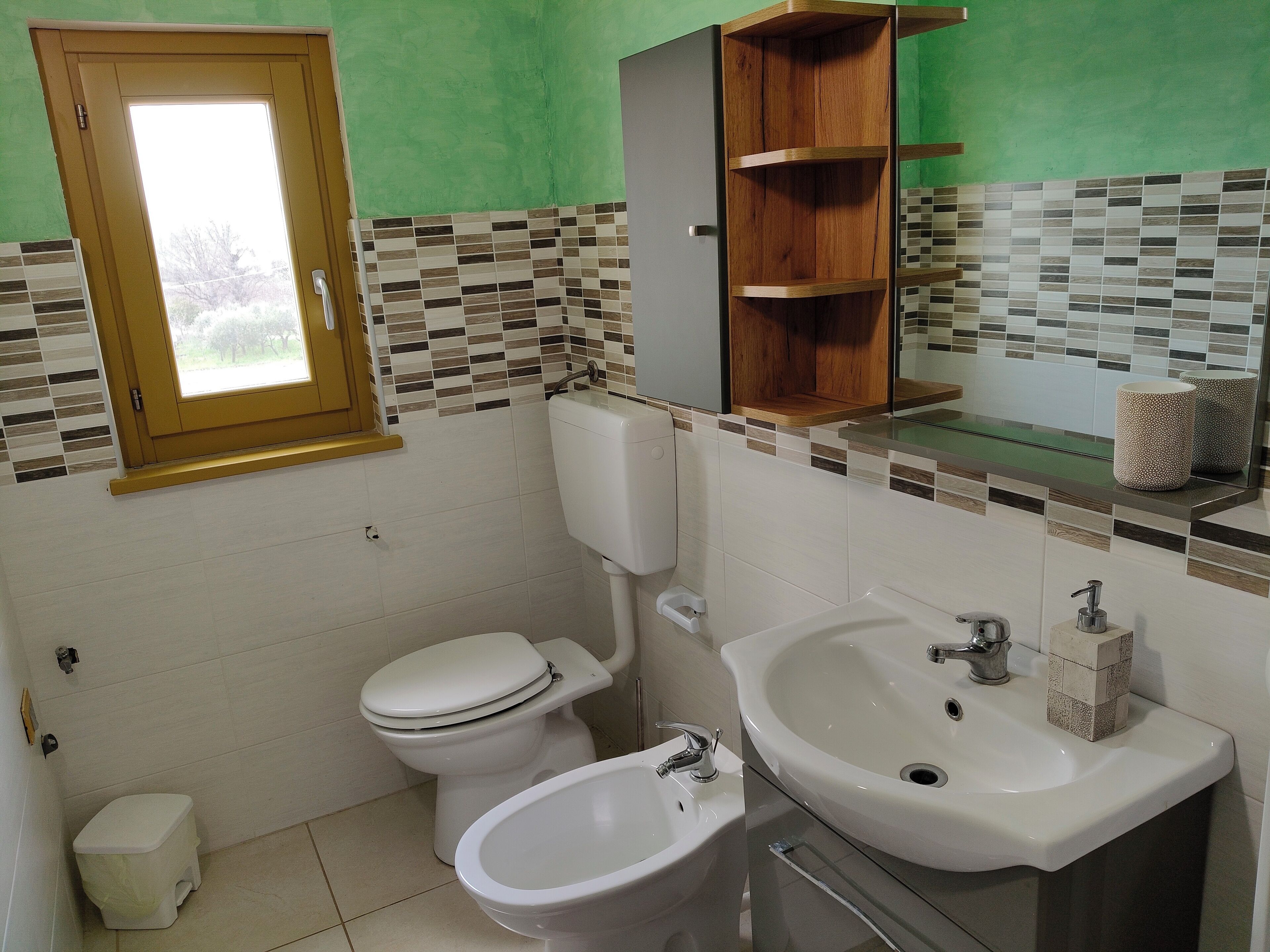 A bathroom with a toilet, bidet, sink, and a window with a wooden frame.