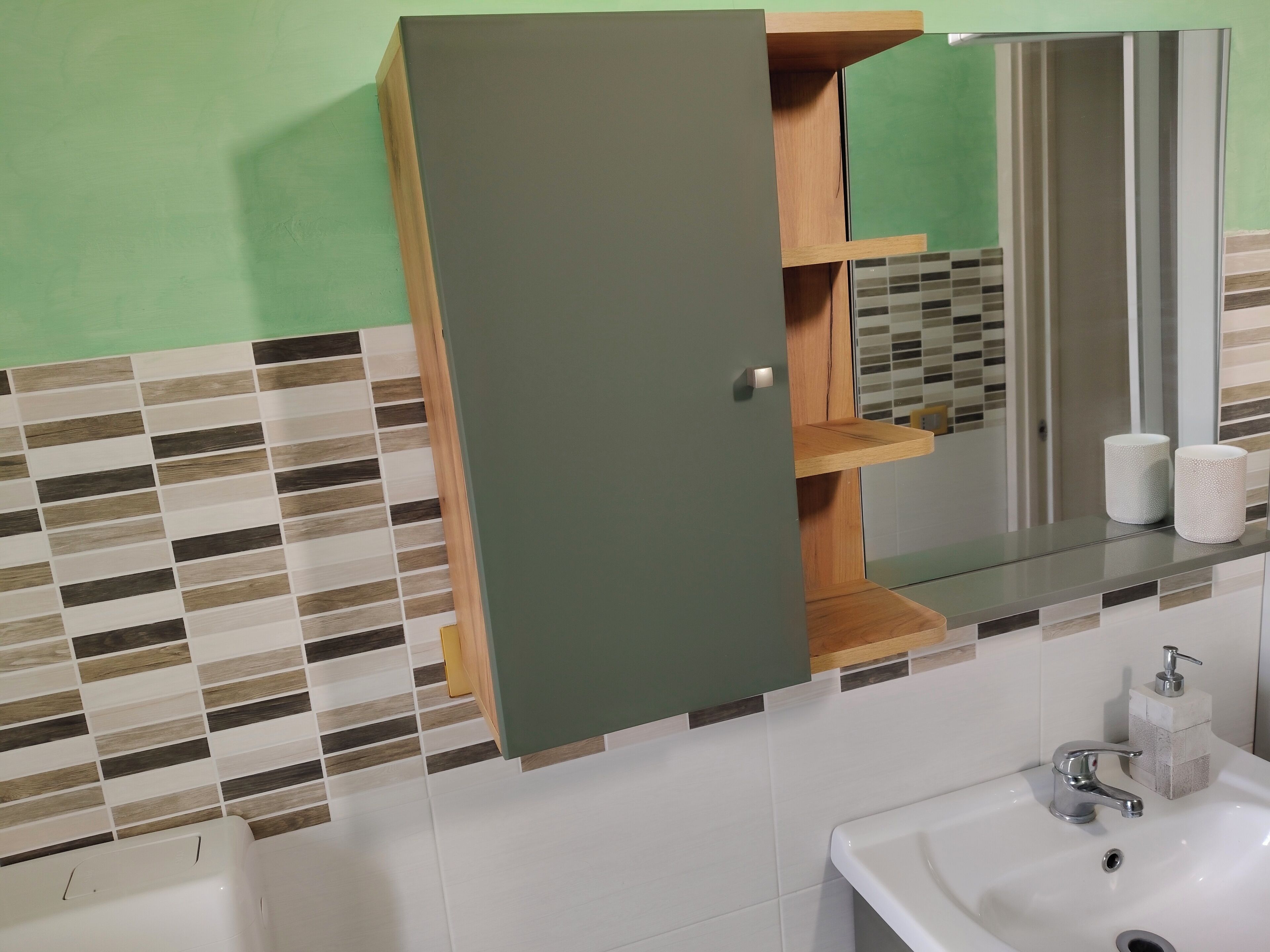 Een badkamer met een groen kastje, een spiegel, een wastafel en een betegelde spatwand.