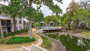 A residential area with a water feature, a wooden bridge, and a pool area. - 2BR Lagoon View Villa - Walk to Coligny (Hilton Head Island)