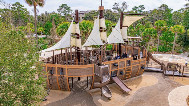 A pirate-themed play structure with slides and climbing areas, surrounded by trees and a sandy ground. - 2BR Lagoon View Villa - Walk to Coligny (Hilton Head Island)